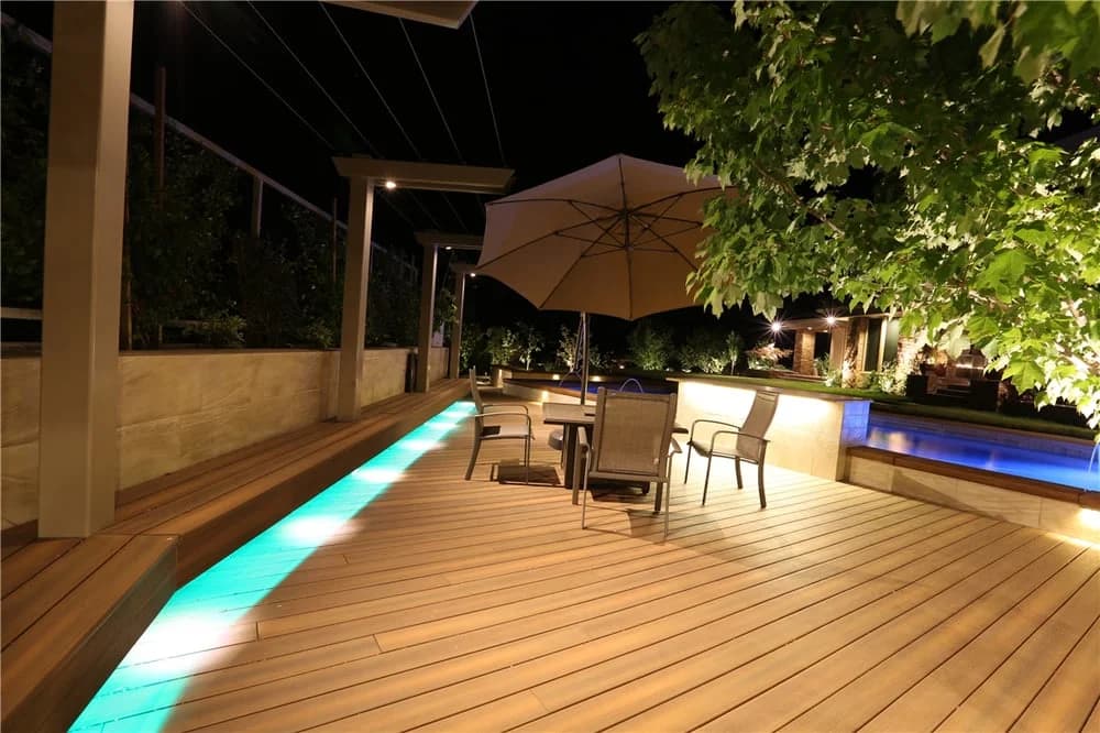 Composite deck with built-in step lighting beside a pool at night, built by Cademartori Construction